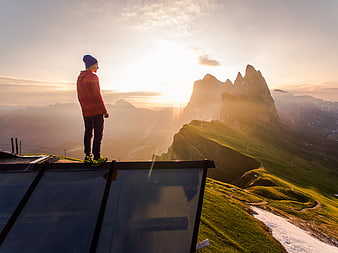 Man standing on glass platform overlooking mountain peaks at sunset
