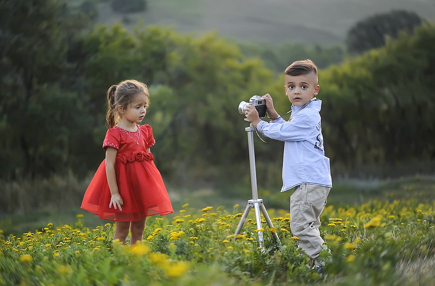 Two children in a field of yellow flowers, boy with vintage camera