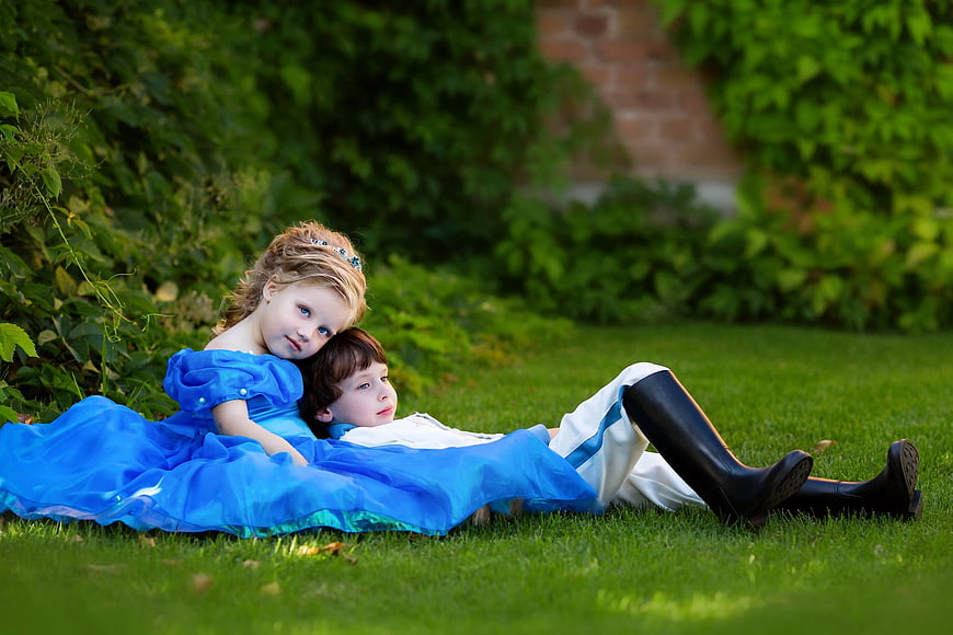 Children dressed as prince and princess lying on grass