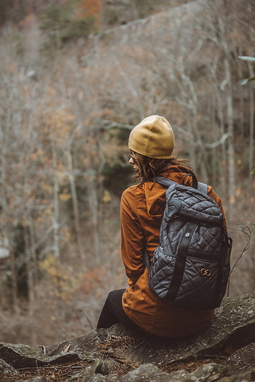 Woman with backpack sitting on rock in autumn forest