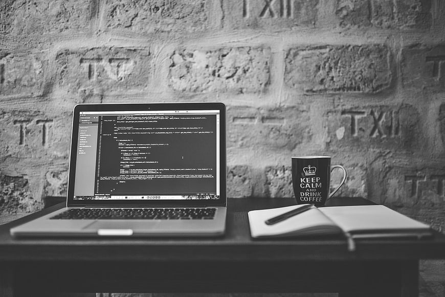 Laptop with code, coffee mug, and notebook on desk