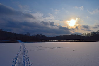 Snowy winter landscape with footprints leading to sunset