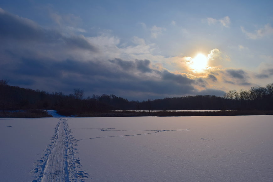 Snowy winter landscape with footprints leading to sunset