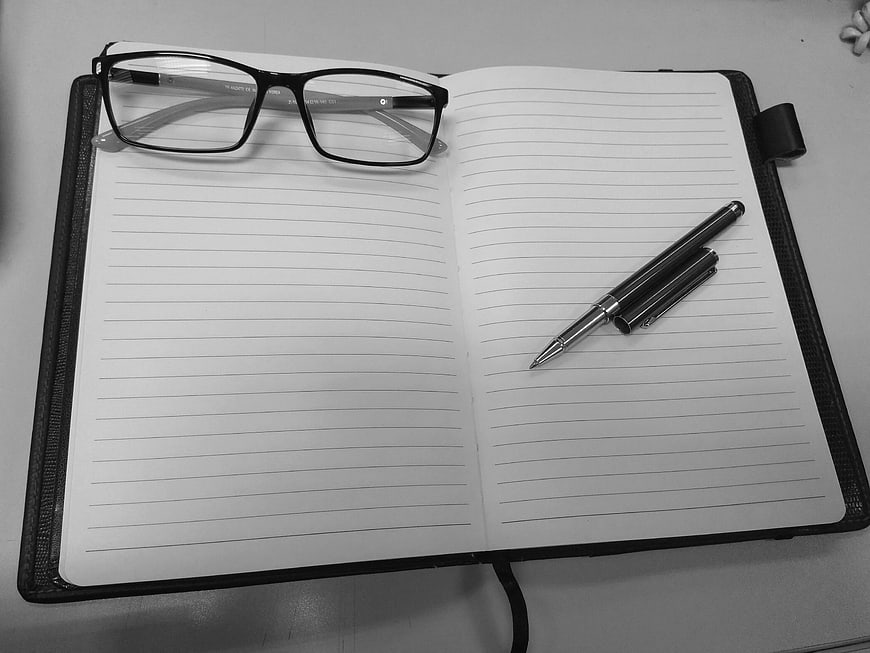 Black and white notebook with glasses and pen on desk
