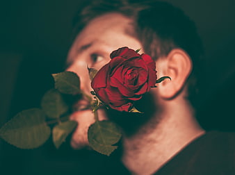 Man holding red rose close to face in moody portrait