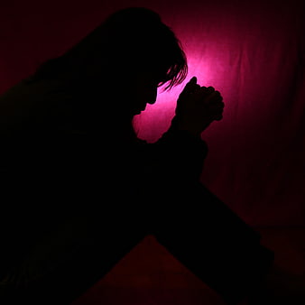 Silhouette of a woman praying in a dark room with red light