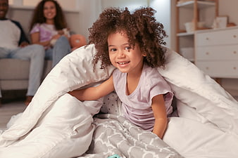 Happy young girl with curly hair playing in a blanket fort