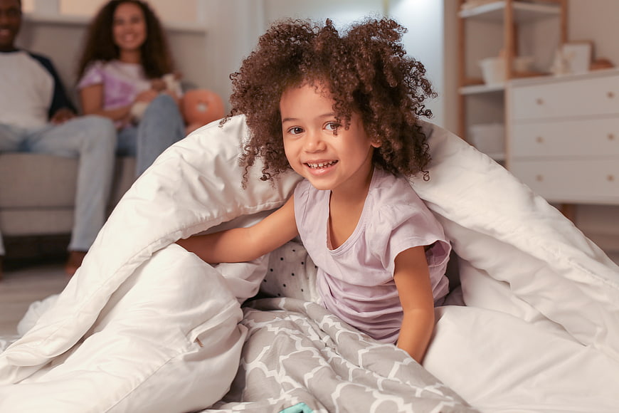 Happy young girl with curly hair playing in a blanket fort