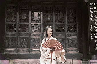Asian woman in traditional hanfu holding fan at ancient architecture