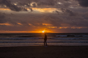 Silhouette of Man Walking on Beach at Sunset