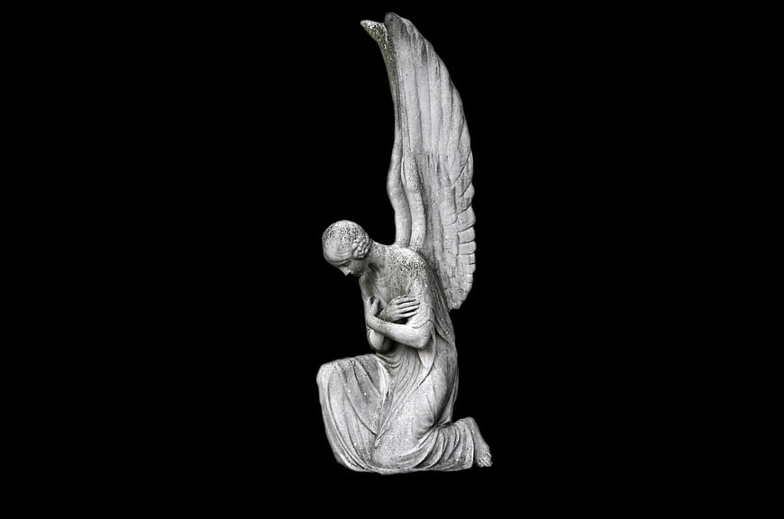 Kneeling stone angel statue with wings on black background