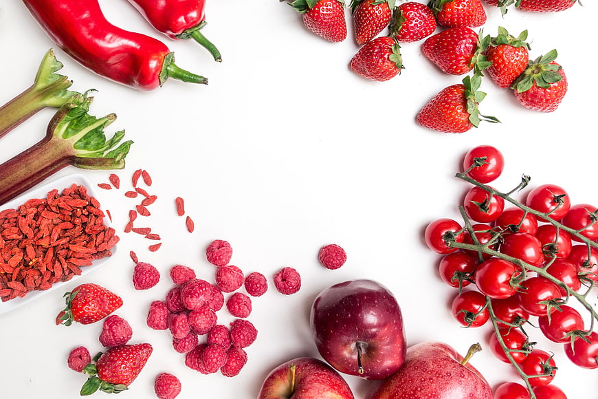 Flat lay of red fruits and vegetables on white background