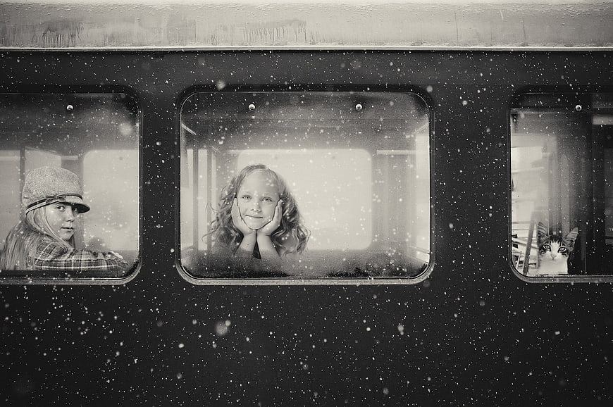 Children and cat looking out of train windows in snow