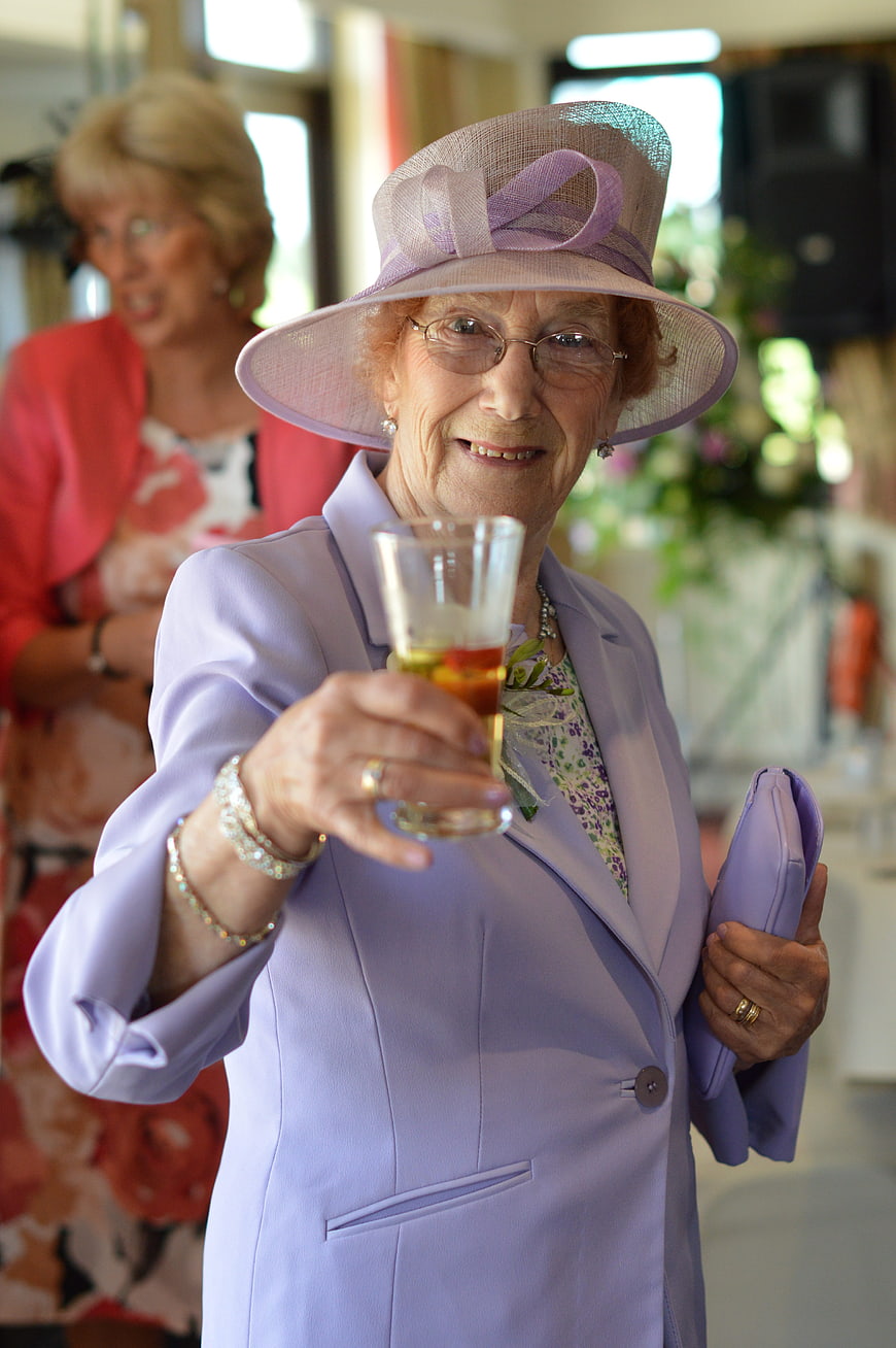Elegant senior woman in lavender hat toasting with a drink at a celebration