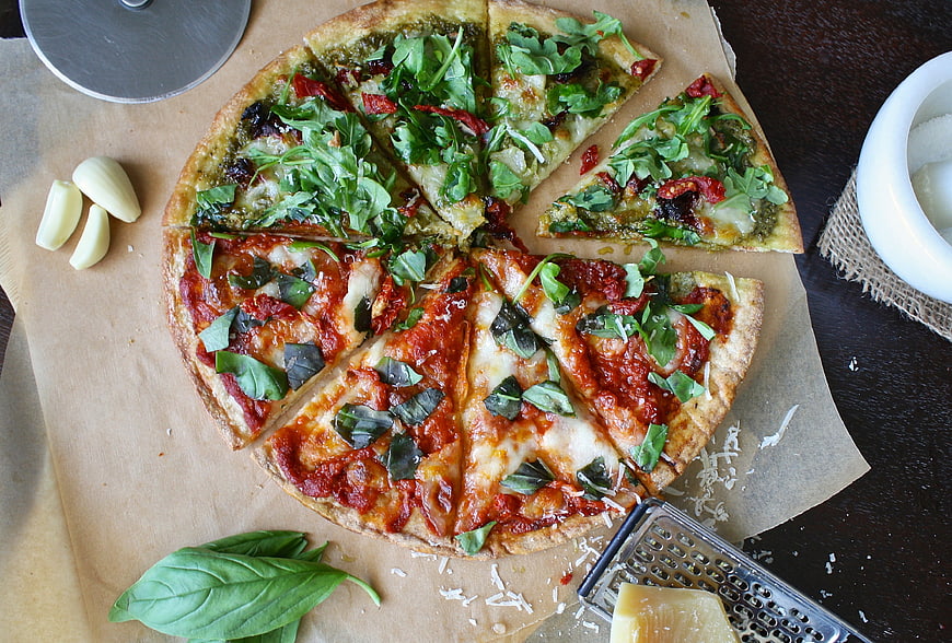 Top view of sliced homemade pizza with pesto and tomato toppings