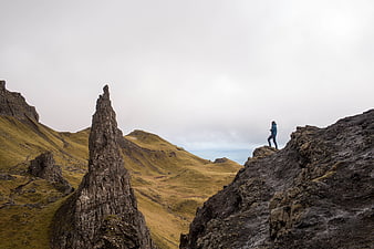 Hiker standing on rocky cliff edge overlooking dramatic mountain landscape