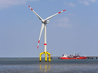 Offshore wind turbine with yellow base and red LNG tanker in background