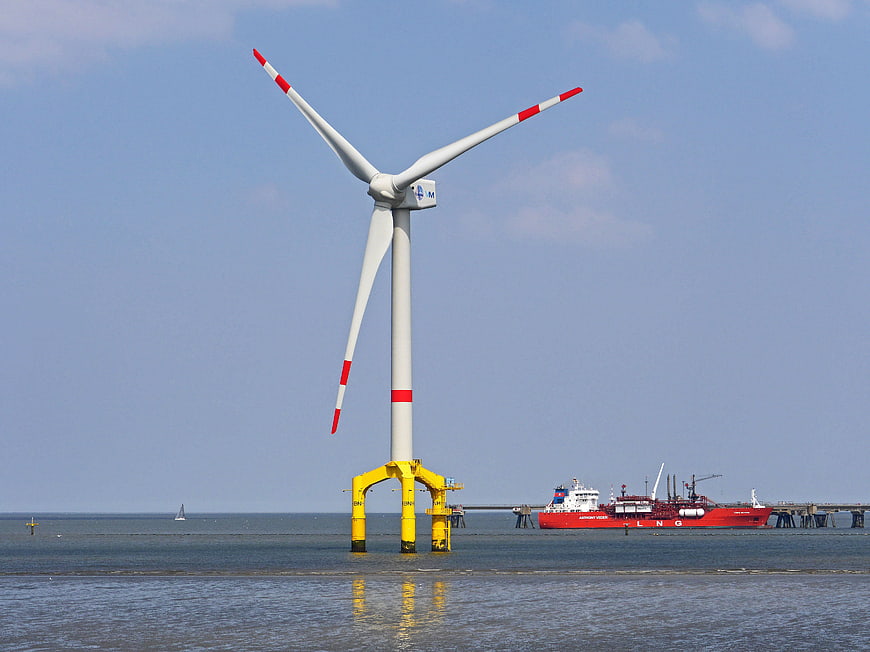 Offshore wind turbine with yellow base and red LNG tanker in background