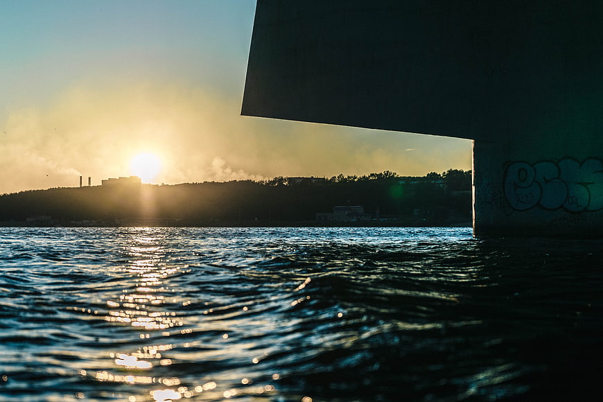 Sunset Reflection on Water Under Concrete Bridge with Graffiti