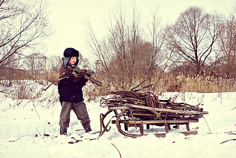 Child pulling wooden sled loaded with firewood in snowy winter landscape