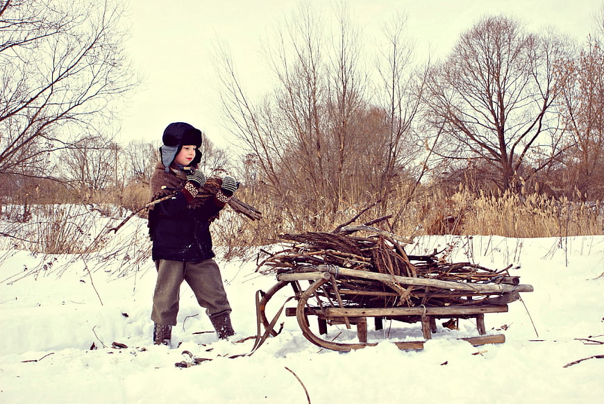 Child pulling wooden sled loaded with firewood in snowy winter landscape