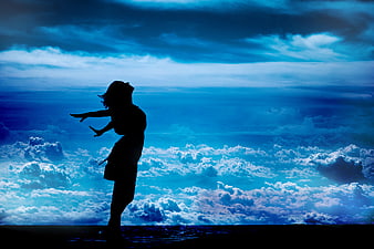 Silhouette of Woman with Arms Outstretched Against Blue Sky