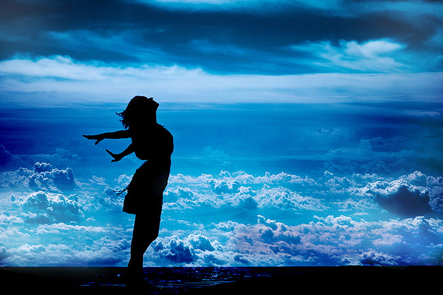 Silhouette of Woman with Arms Outstretched Against Blue Sky
