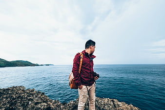 Man with Camera Standing on Rocky Cliff Overlooking Ocean