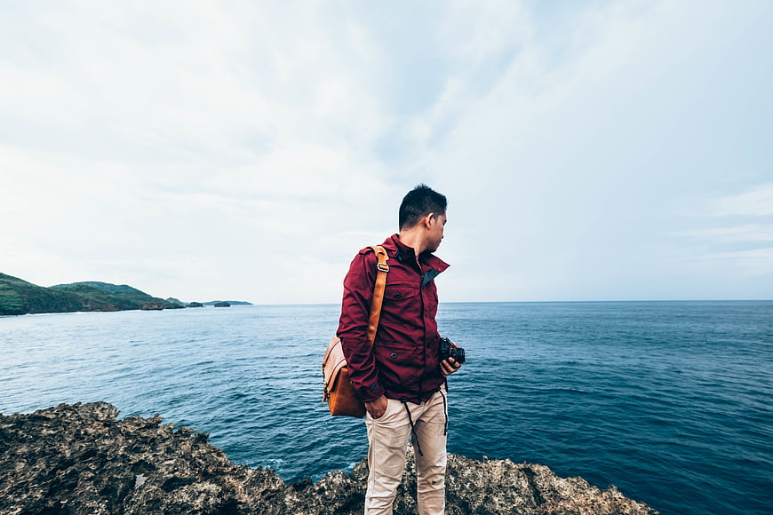 Man with Camera Standing on Rocky Cliff Overlooking Ocean
