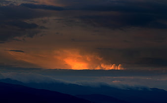 Dramatic sunset breaking through dark storm clouds over mountains
