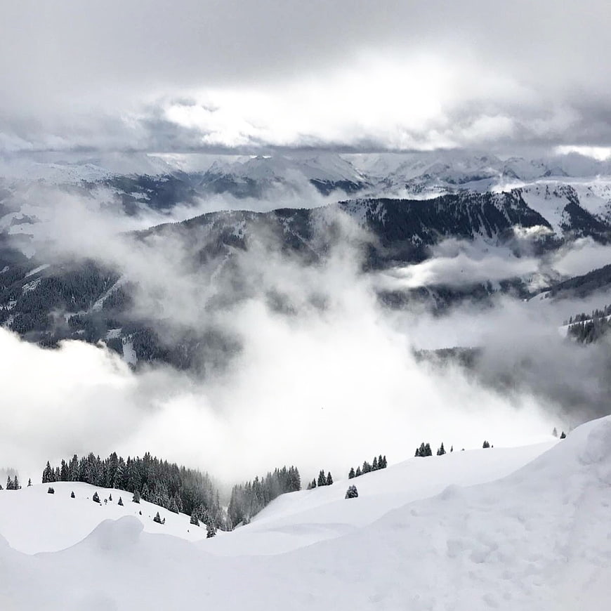 Snowy mountain landscape with clouds and pine trees