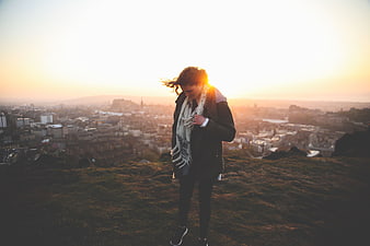 Woman standing on hill overlooking city at sunset