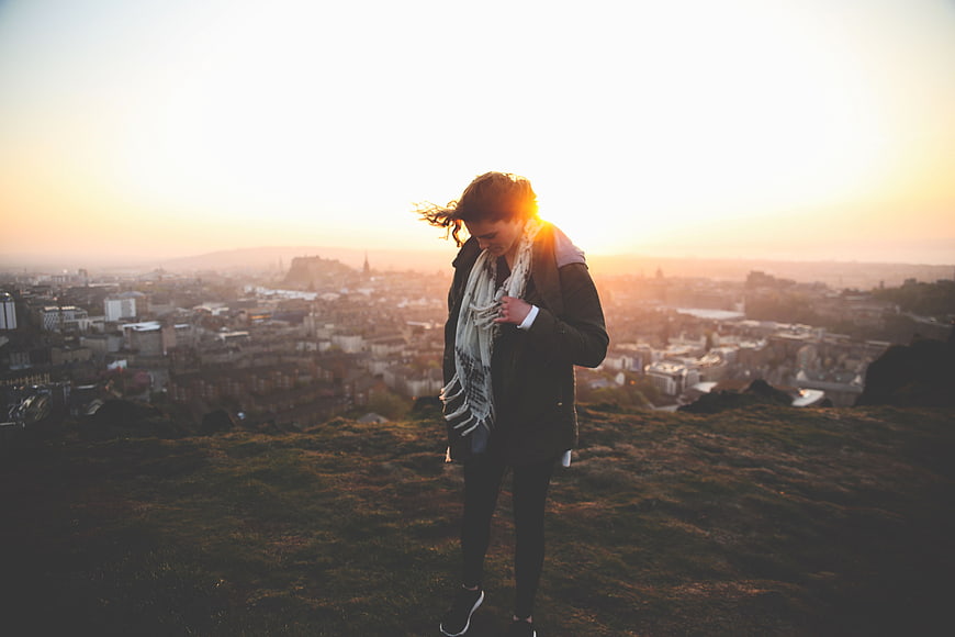 Woman standing on hill overlooking city at sunset