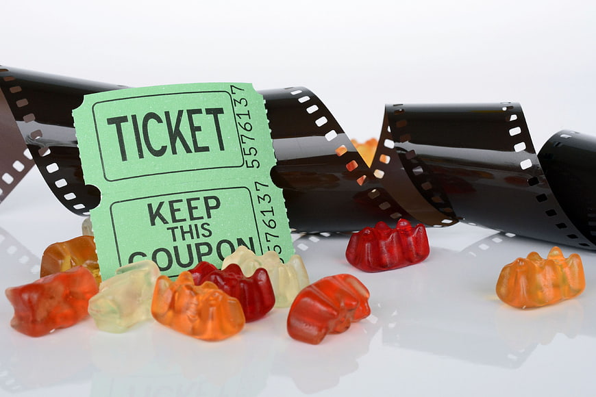 Movie ticket and gummy bears with film strip on white background