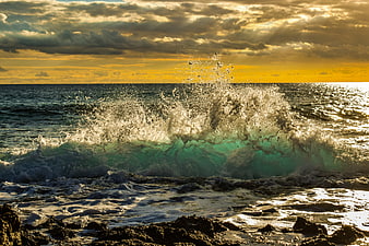 Dramatic ocean wave crashing on rocky shore at golden hour