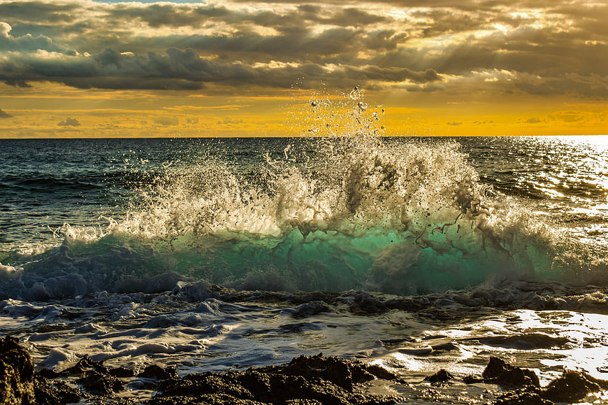 Dramatic ocean wave crashing on rocky shore at golden hour