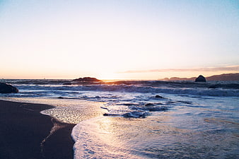 Serene Sunset Ocean Waves on Sandy Beach with Rocks
