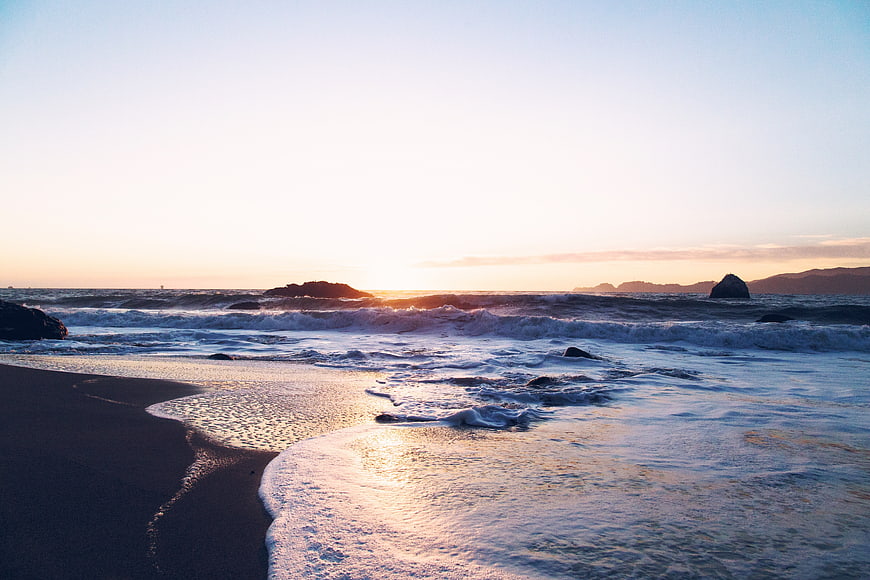 Serene Sunset Ocean Waves on Sandy Beach with Rocks