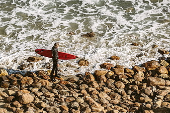 Surfer with Red Board on Rocky Shore