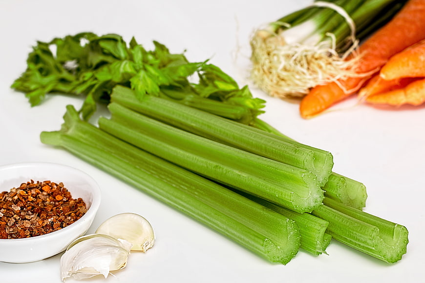 Fresh celery stalks with carrots, garlic, and spices on white background