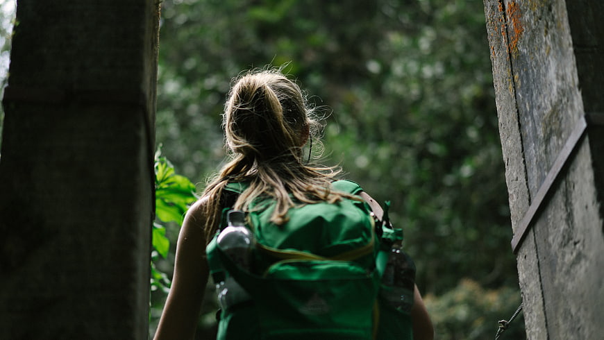 Woman with Green Backpack Hiking Through Forest Ruins