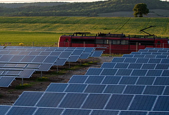 Solar panels in foreground with red electric train passing through green fields