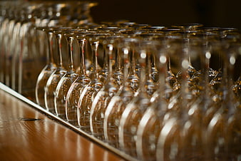 Rows of empty wine glasses on a wooden bar counter