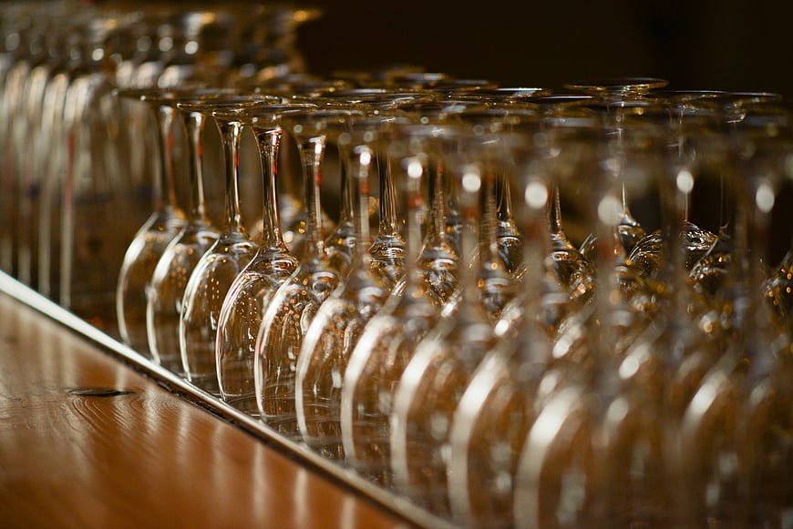 Rows of empty wine glasses on a wooden bar counter