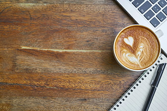 Flat lay of cappuccino, laptop, and notebook on wooden desk