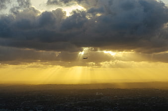 Airplane Silhouette Flying Through Golden Sunbeams Over City