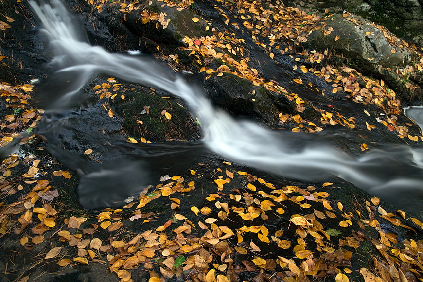 Autumn stream with long exposure water flow over black rocks