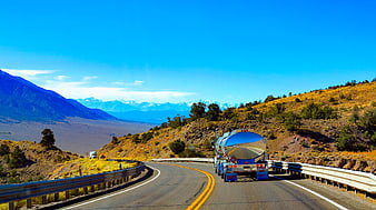 Tanker truck driving on winding mountain highway with blue sky