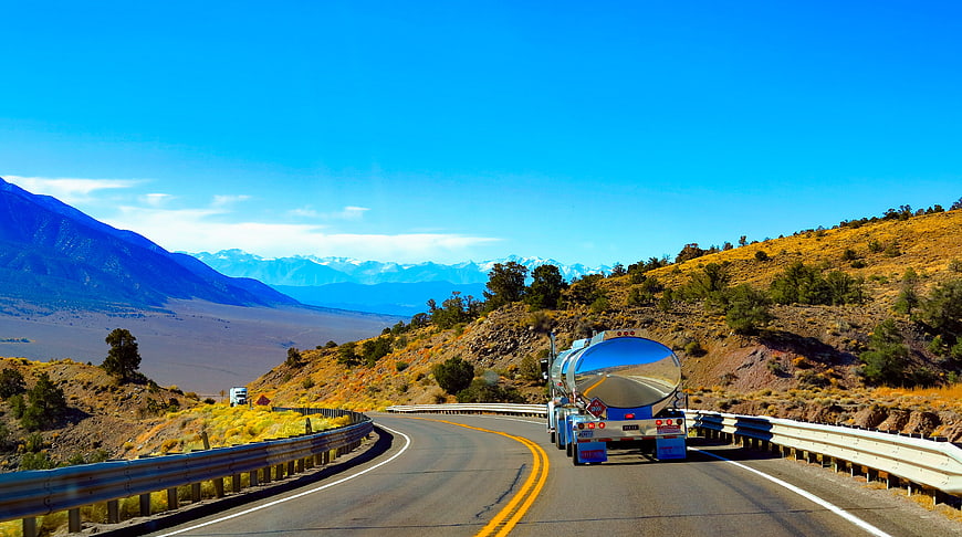 Tanker truck driving on winding mountain highway with blue sky