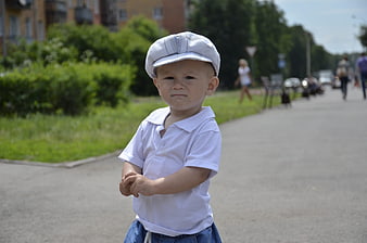 Cute toddler boy in white cap standing on sunny path